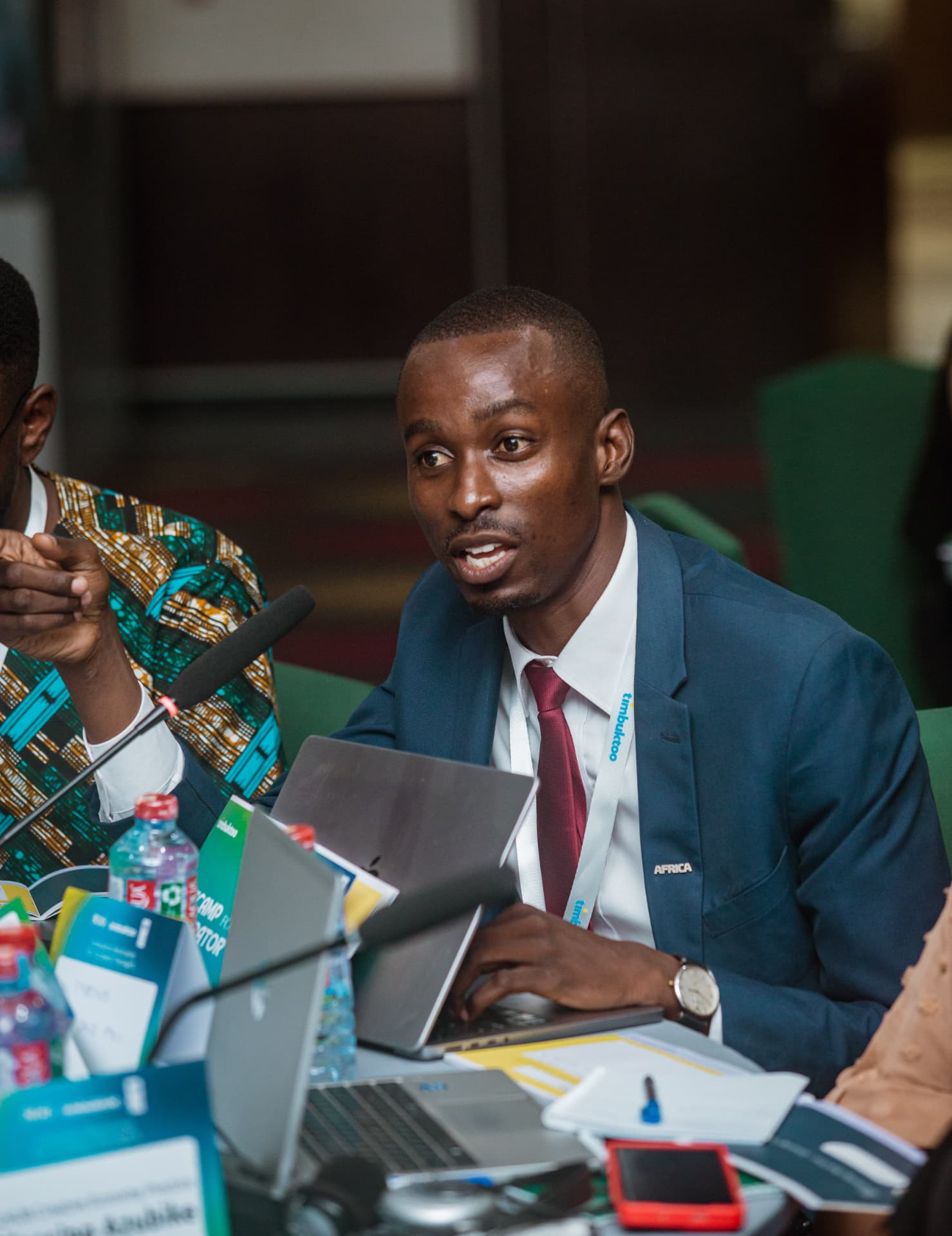King David Amo speaking from a panel table with a microphone and laptop