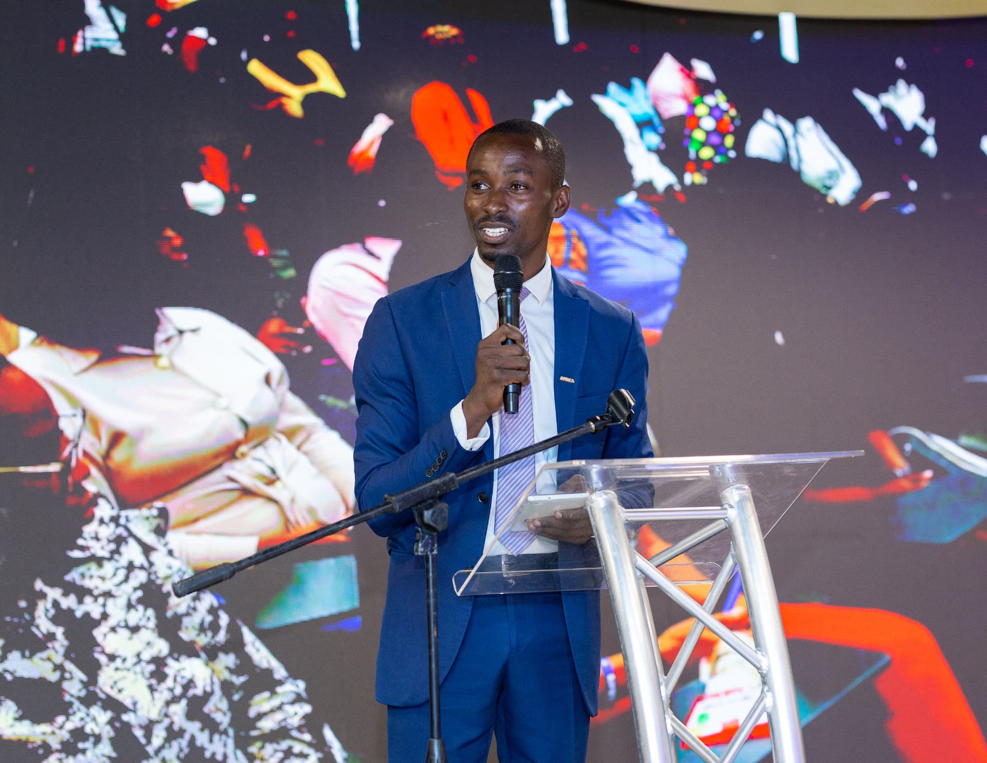 King David Amo speaking into a microphone at a podium in front of a digital event backdrop
