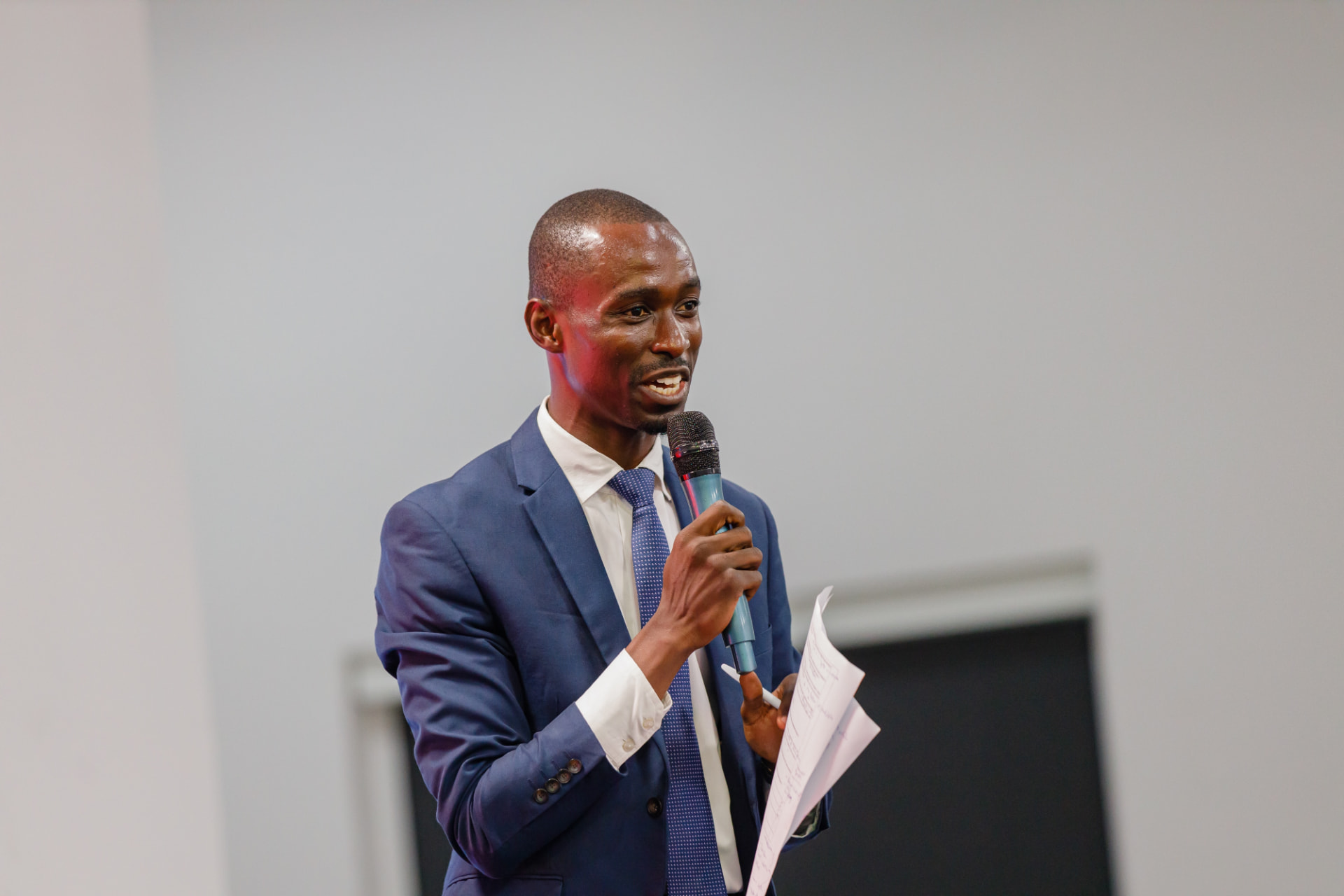 King David Amo speaking on stage with a microphone and prepared notes
